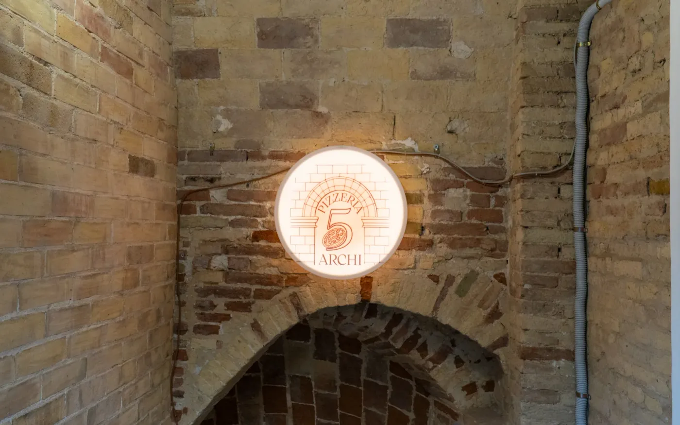 Insegna luminosa storica di Pizzeria 5 Archi incastonata nell'arco in mattoni a vista